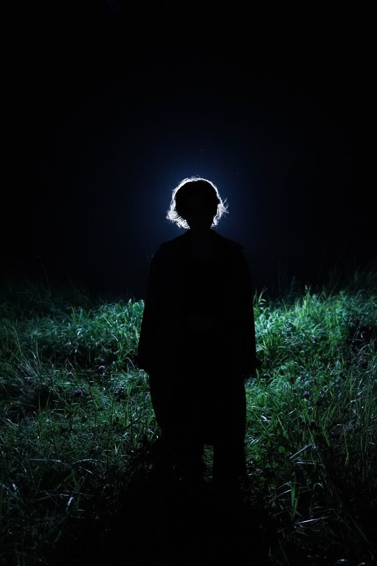 Backlit figure standing in night grass, face in shadow