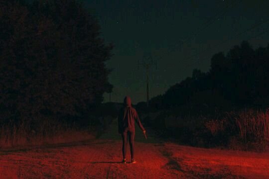 Hooded figure on a road washed in red light