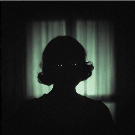 Silhouette with faintly glinting eyes against green curtains